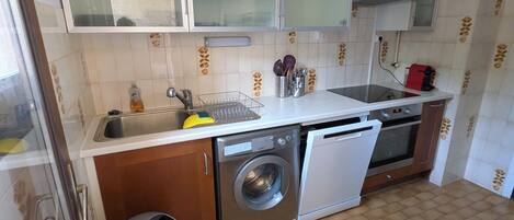 Cocina compacta con lavadora, lavavajillas y una pequeña zona de fregadero.