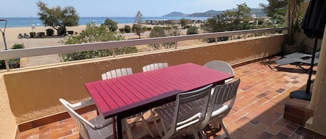 A terrace with a table and chairs, overlooking a beach and the sea.