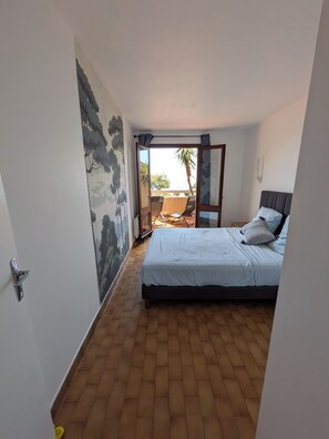 Quarto com cama, vista para o exterior e porta que dá para uma varanda.