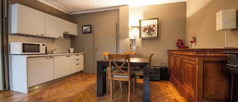 A compact kitchen with white cabinets, a microwave, and a dining table with chairs.