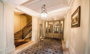 A hallway with a stone floor, a staircase, and a door leading to a room. - CHARMING & SPACIOUS STUDIO STEPS FROM LUXEMBOURG GARDENS (Paris)