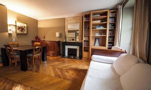 A living room with a fireplace, a dining area, a sofa, and a bookshelf. - CHARMING & SPACIOUS STUDIO STEPS FROM LUXEMBOURG GARDENS (Paris)