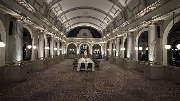 A grand hall with a high arched ceiling, marble columns, and a patterned carpet.
