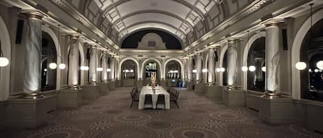 A grand hall with a high arched ceiling, marble columns, and a patterned carpet.