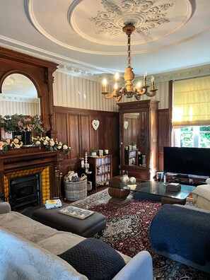 Un salon traditionnel avec une cheminée, des étagères à livres, un téléviseur et un lustre.