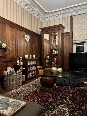 Ein traditionell eingerichtetes Wohnzimmer mit Kamin, Bücherregalen, einem Fernseher und einem großen Spiegel.