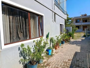 A building with a paved walkway, potted plants, and a window with curtains. - Rezidenca Pahumi  (Durrës)