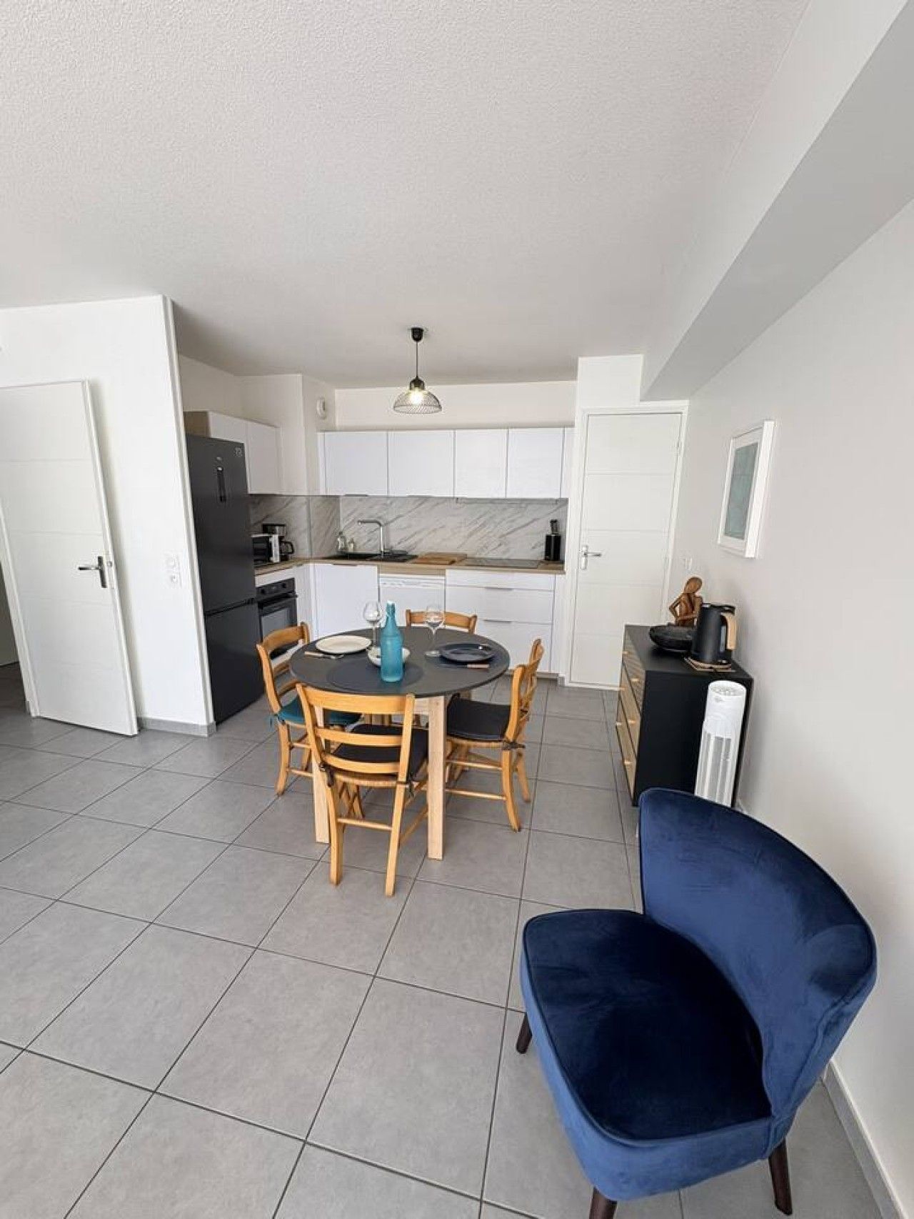 A compact kitchen with white cabinets, a dining table with chairs, and a blue chair in the foreground.