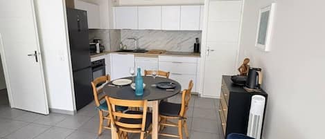 Cocina compacta con armarios blancos, una mesa de comedor con sillas y una silla azul en primer plano.