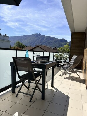 A balcony with a dining table and chairs, a bottle, and glasses, overlooking a mountainous landscape. - 49-square-meter apartment, 1 bedroom, terrace, and parking space (Aix-les-Bains)