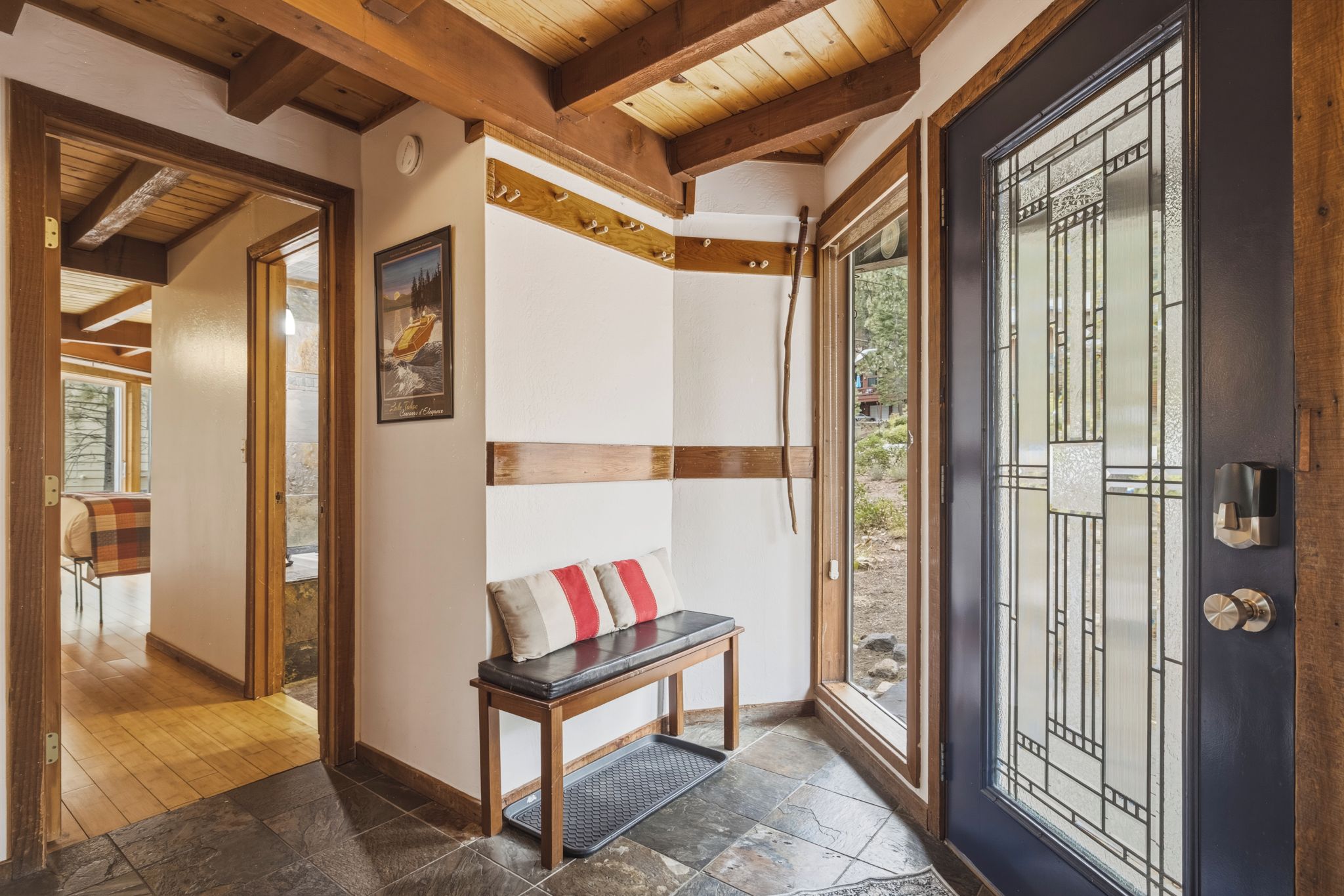 A hallway with a bench, a door with a glass panel, and a framed picture on the wall.