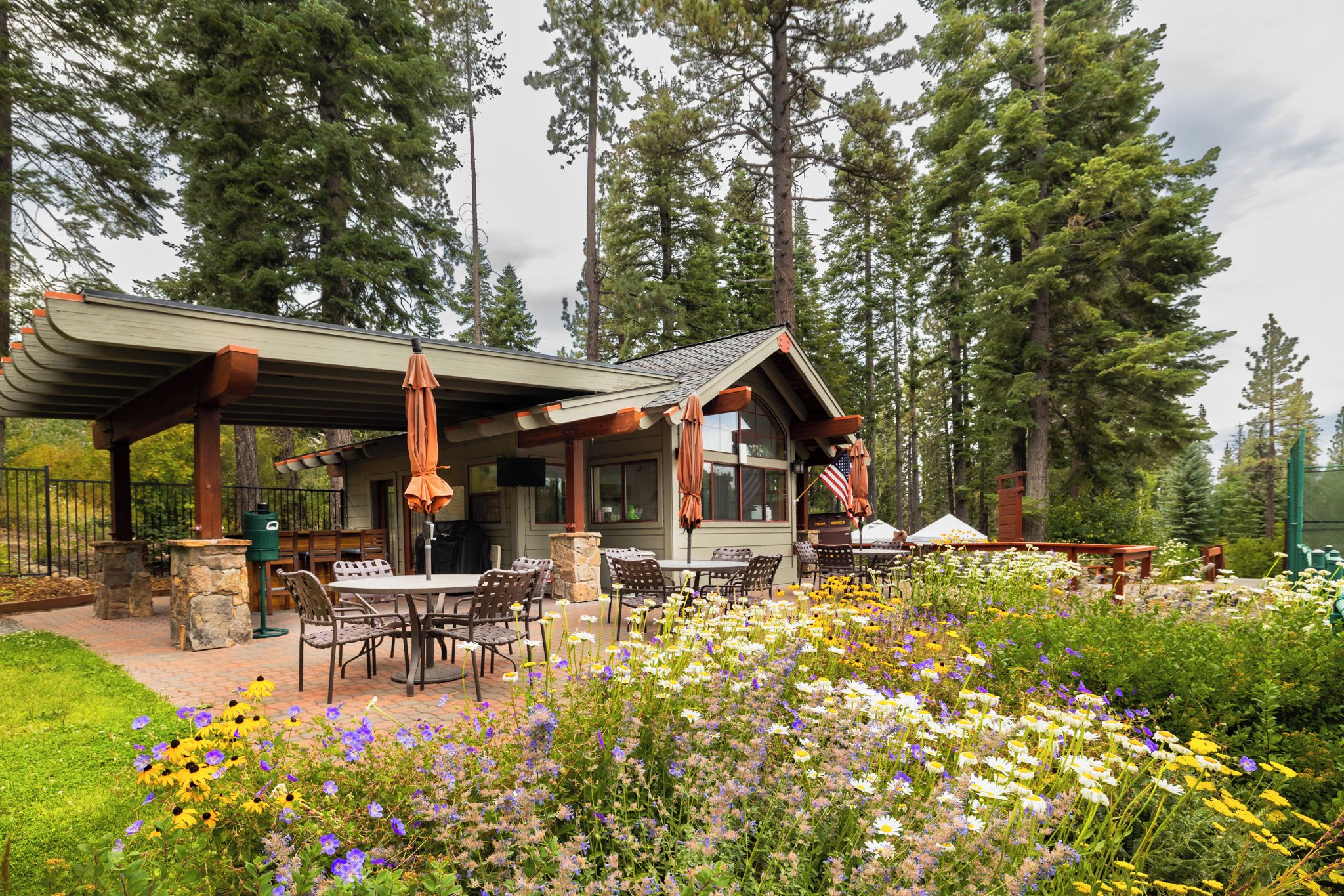 Eine Lodge mit Sitzgelegenheit im Freien, umgeben von einem Garten mit verschiedenen Blumen und hohen Bäumen.