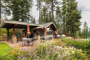 Eine Lodge mit Sitzgelegenheit im Freien, umgeben von einem Garten mit verschiedenen Blumen und hohen Bäumen.