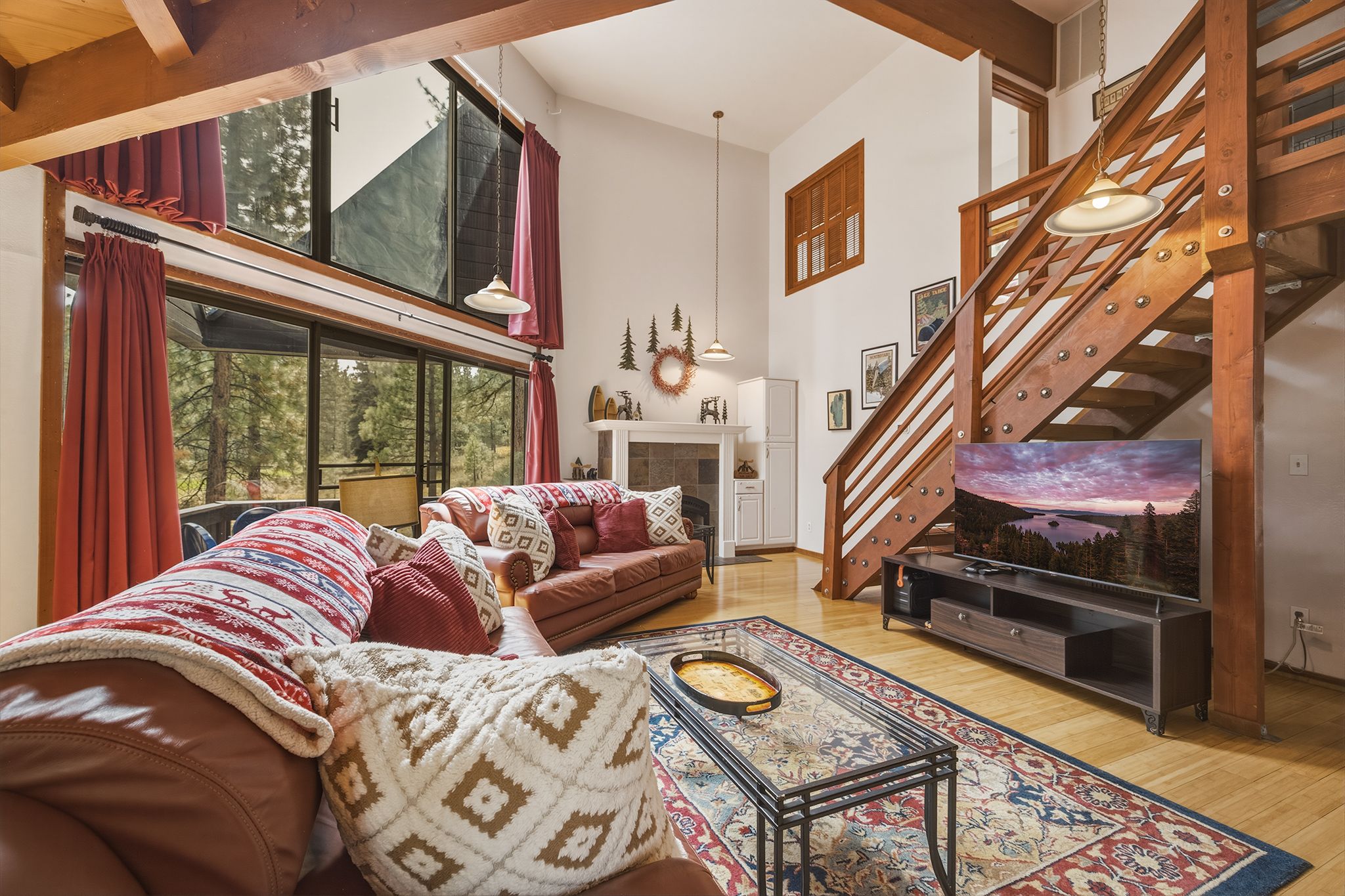 Una sala de estar acogedora con chimenea, una escalera y un ventanal con vistas a un bosque.