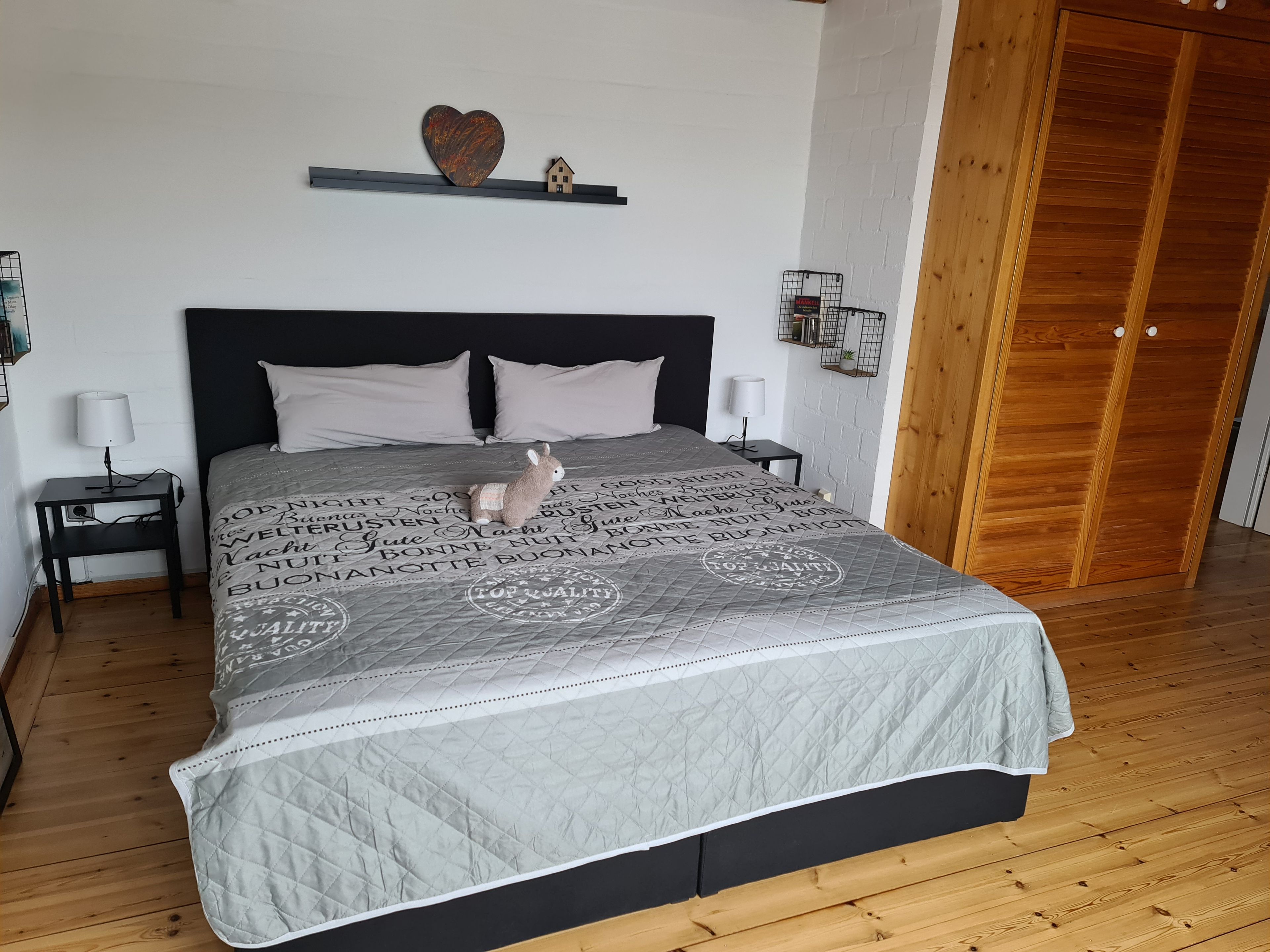 Un lit avec une couverture matelassée, un petit animal en peluche et un décor en forme de cœur accroché au mur.