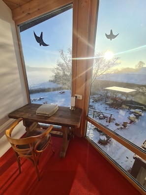 A room with a wooden table and chair, a laptop, and a view of a snowy landscape through a large window. - Familienglück - Die "AusZeit" vom Alltag (Schönberg)
