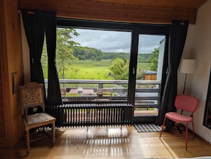 A room with a large window, a wooden floor, a radiator, a small table with a chair, and a lamp. - Familienglück - Die "AusZeit" vom Alltag (Schönberg)