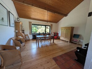Una habitació àmplia amb sostre de fusta, taula de dinar amb cadires, un butacó vermell, un armari i una pissarra.