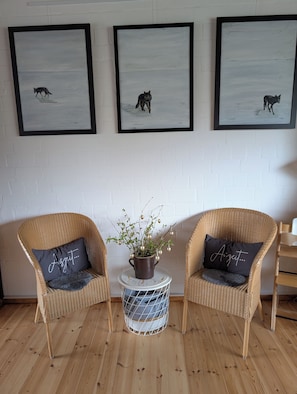 A room with three framed animal prints on the wall, two wicker chairs with cushions, and a small round table with a plant and a basket. - Familienglück - Die "AusZeit" vom Alltag (Schönberg)