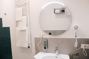 Un baño con un espejo redondo, toallero, lavamanos y secador de pelo.