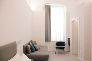 Una habitación moderna y minimalista con un sofá gris, una silla negra y un ventanal con cortinas.