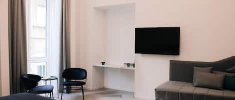 Habitación de hotel con cama, sofá, televisión montada en la pared y una pequeña mesa con sillas.