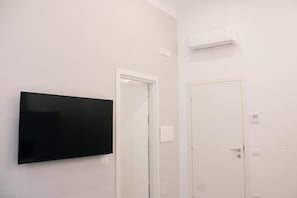 A room with a flat-screen TV mounted on the wall, a white door, and an air conditioning unit. - Six Luxury Rooms Quartieri Spagnoli (Naples)