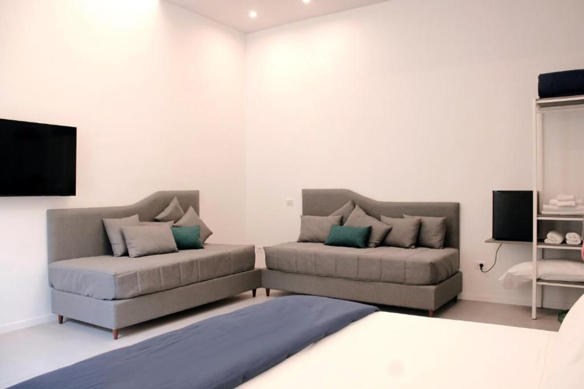 Un dormitorio moderno con dos sofás, una cama, un televisor y un armario.