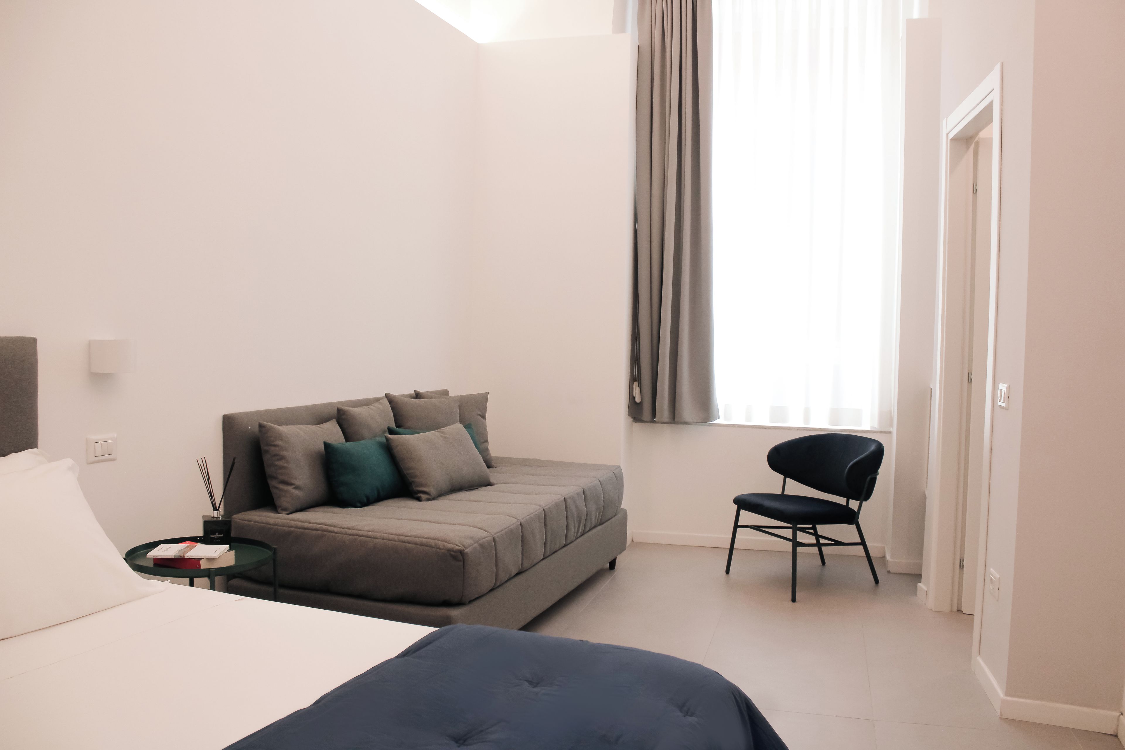 Ein modernes Hotelzimmer mit Bett, Sofa, Sessel und einem Fenster mit Vorhängen.