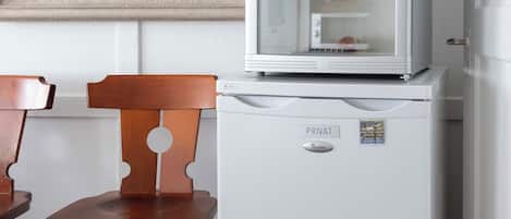 A white refrigerator with a glass door, a wooden chair, and a painting on the wall.