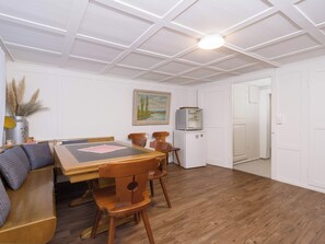 Un comedor con una mesa de madera, sillas y un banco. Hay un cuadro en la pared y un refrigerador en la esquina.