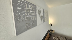 A room with a bed, a wall-mounted artwork, and a floor lamp.