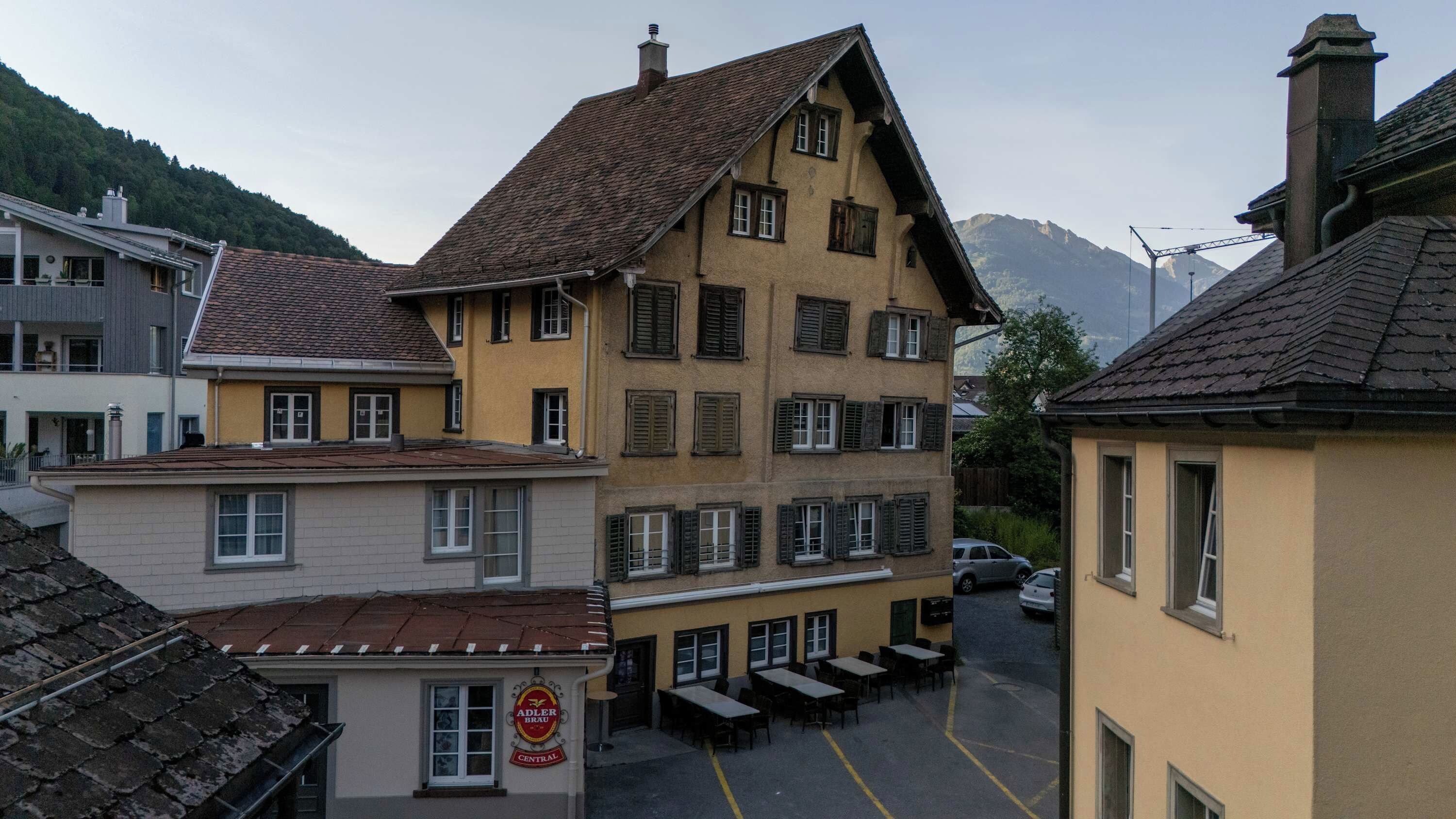 Un edificio de varios pisos con un patio central, que cuenta con un restaurante llamado 'Adler Brau Central' y mesas al aire libre.