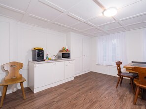 Ett kök med vita skåp, en mikrovågsugn, en kaffebryggare och en matplats med ett träbord och stolar.