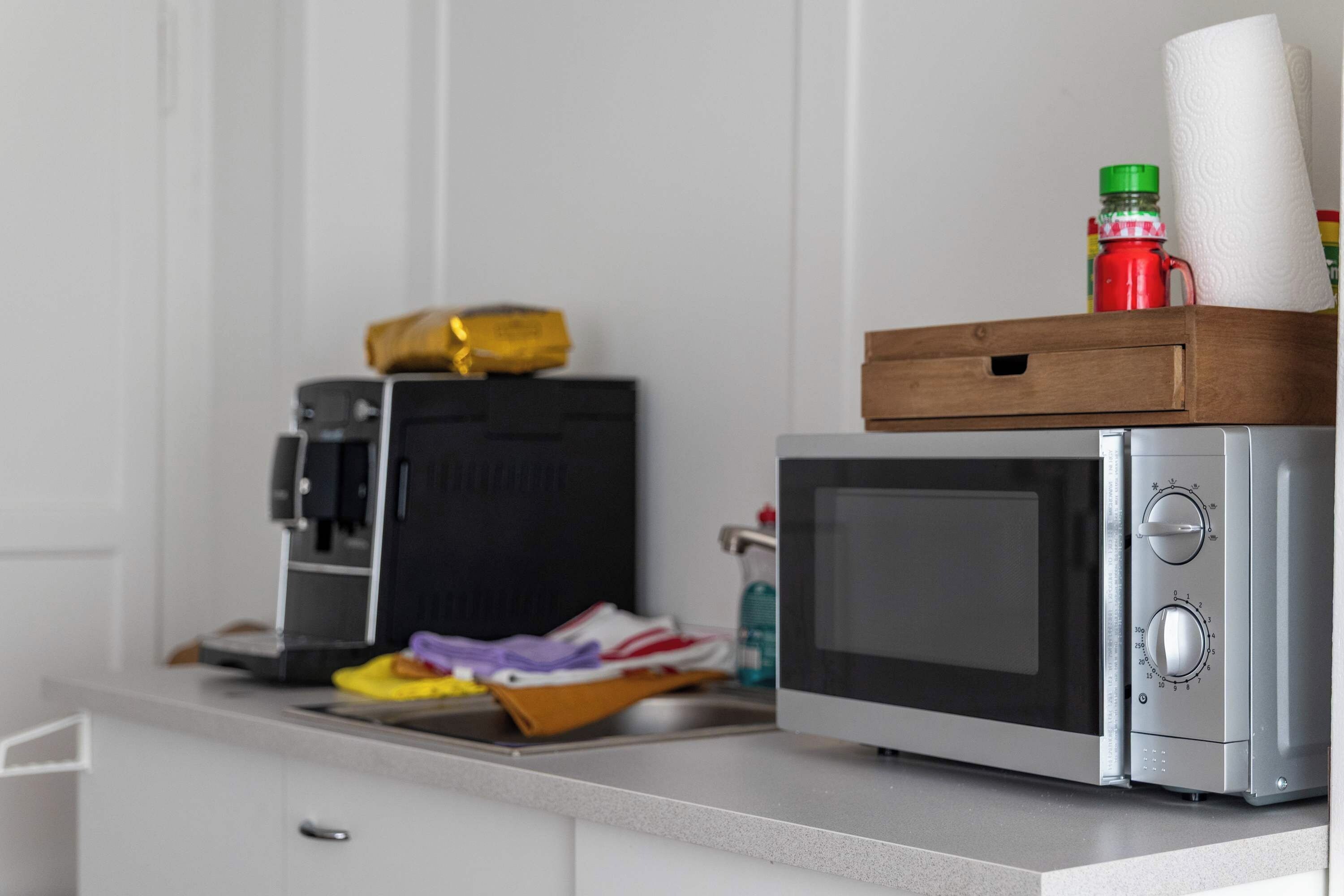 A kitchen with a microwave, a coffee maker, and a box containing a bottle and a roll of paper towels.