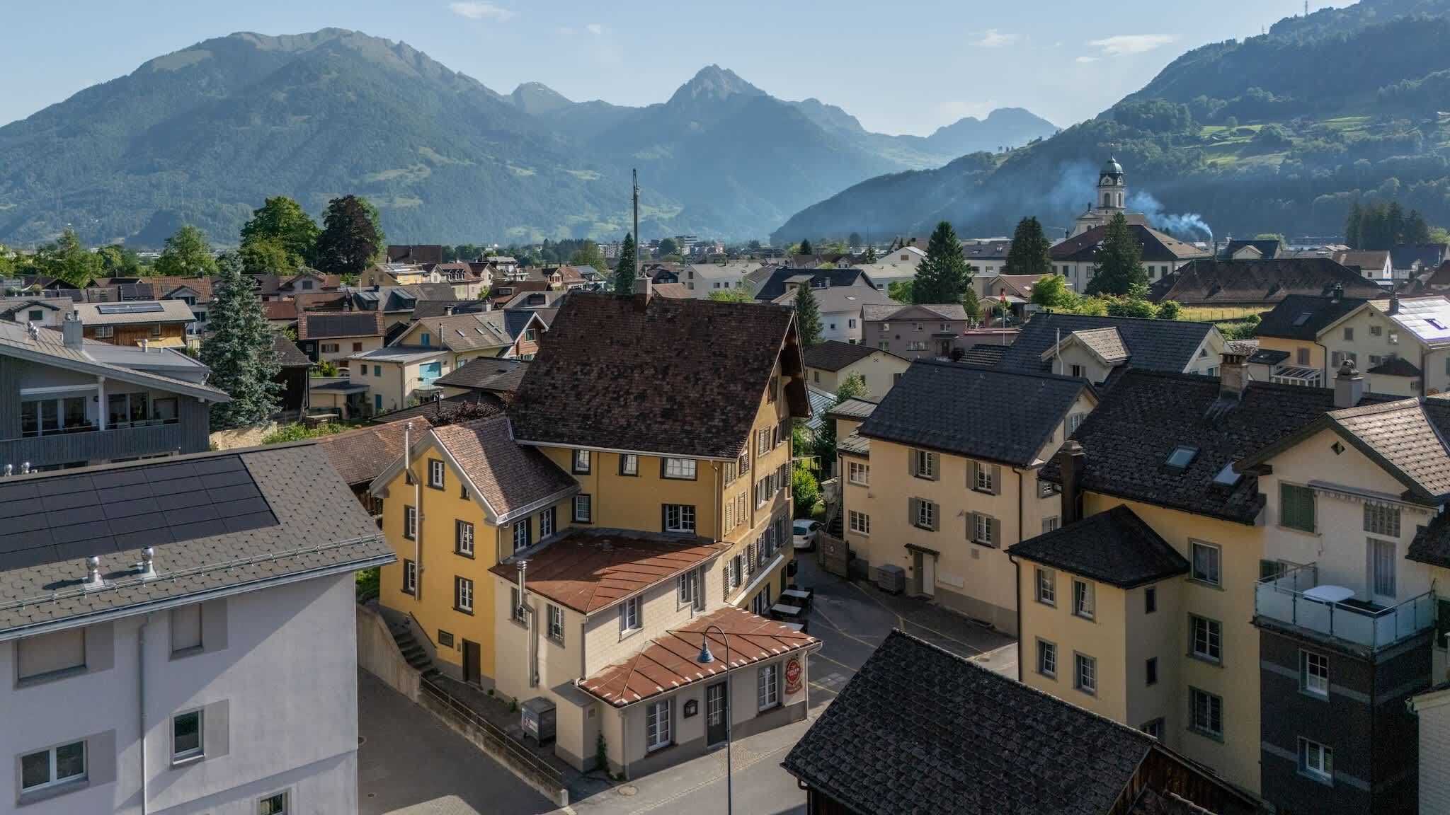 Une ville à l’architecture traditionnelle, une église surmontée d’un dôme, et des montagnes en arrière-plan.