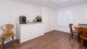 A kitchen with white cabinets, a microwave, a coffee maker, and a dining area with a wooden table and chairs.