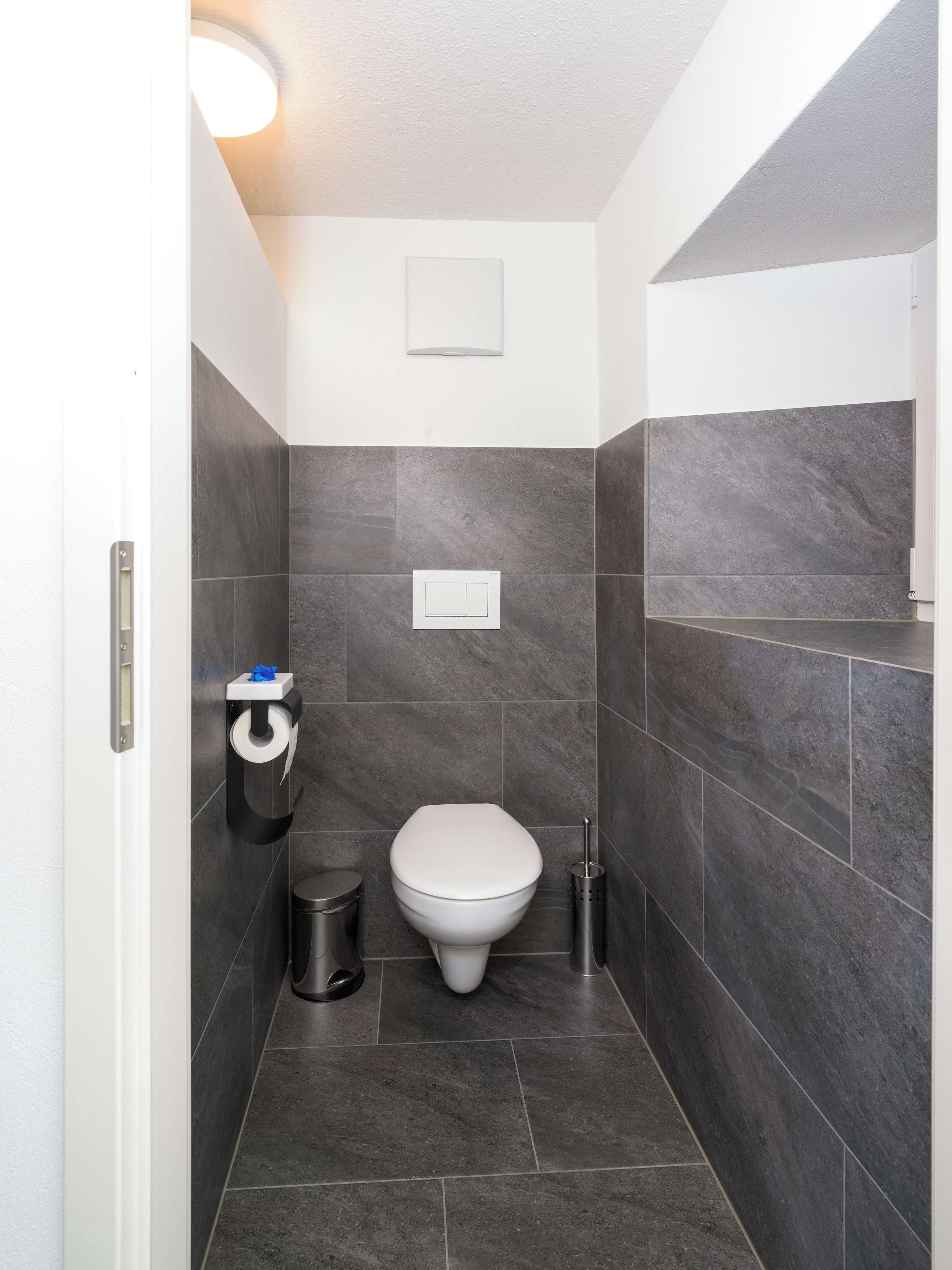 Ein kleines, modernes Badezimmer mit Toilette, Mülleimer und Toilettenpapierhalter.