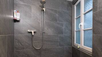 Ein modernes Duschbad mit dunklen Fliesen, einer Handbrause und einem gläsernen Fenster.