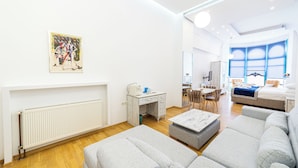 Una sala moderna con un radiador blanco, sofás grises, una cafetera y un cuadro en la pared.
