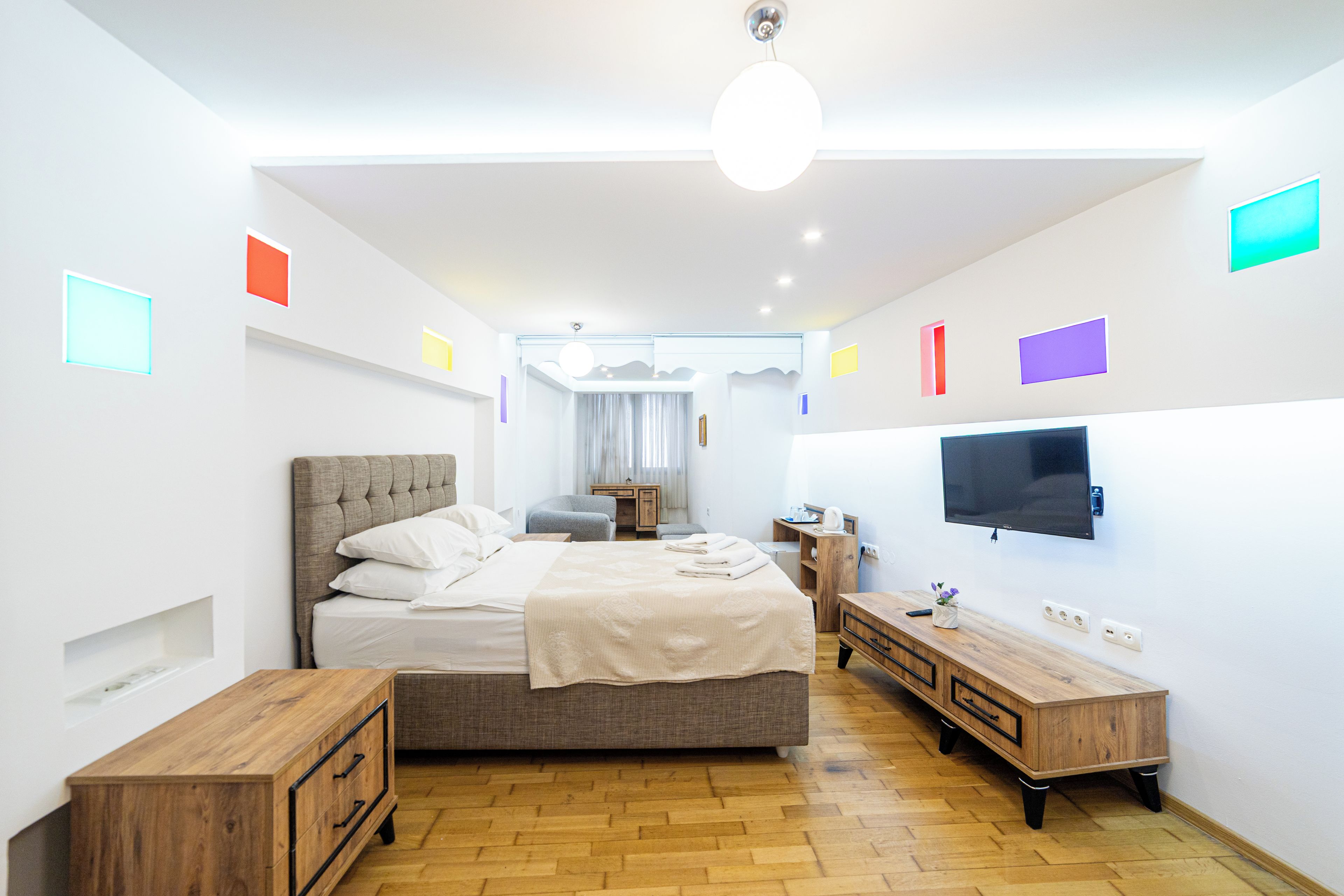 Ein modernes Hotelzimmer mit einem großen Bett, Nachttischen, einem Fernseher und einer Holzkommode.
