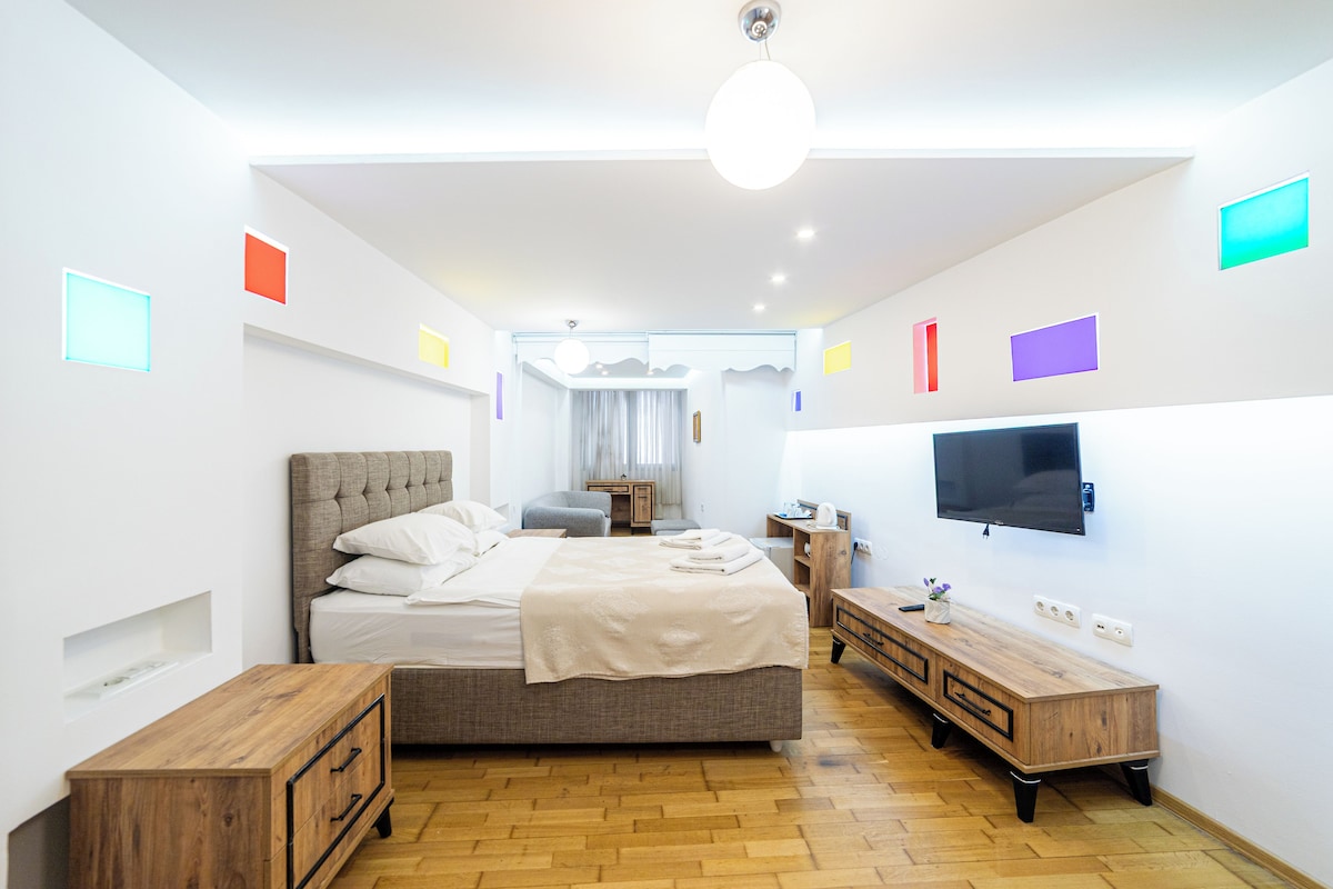 A modern hotel room with a large bed, bedside tables, a TV, and a wooden dresser.