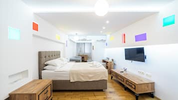 A modern hotel room with a large bed, bedside tables, a TV, and a wooden dresser.