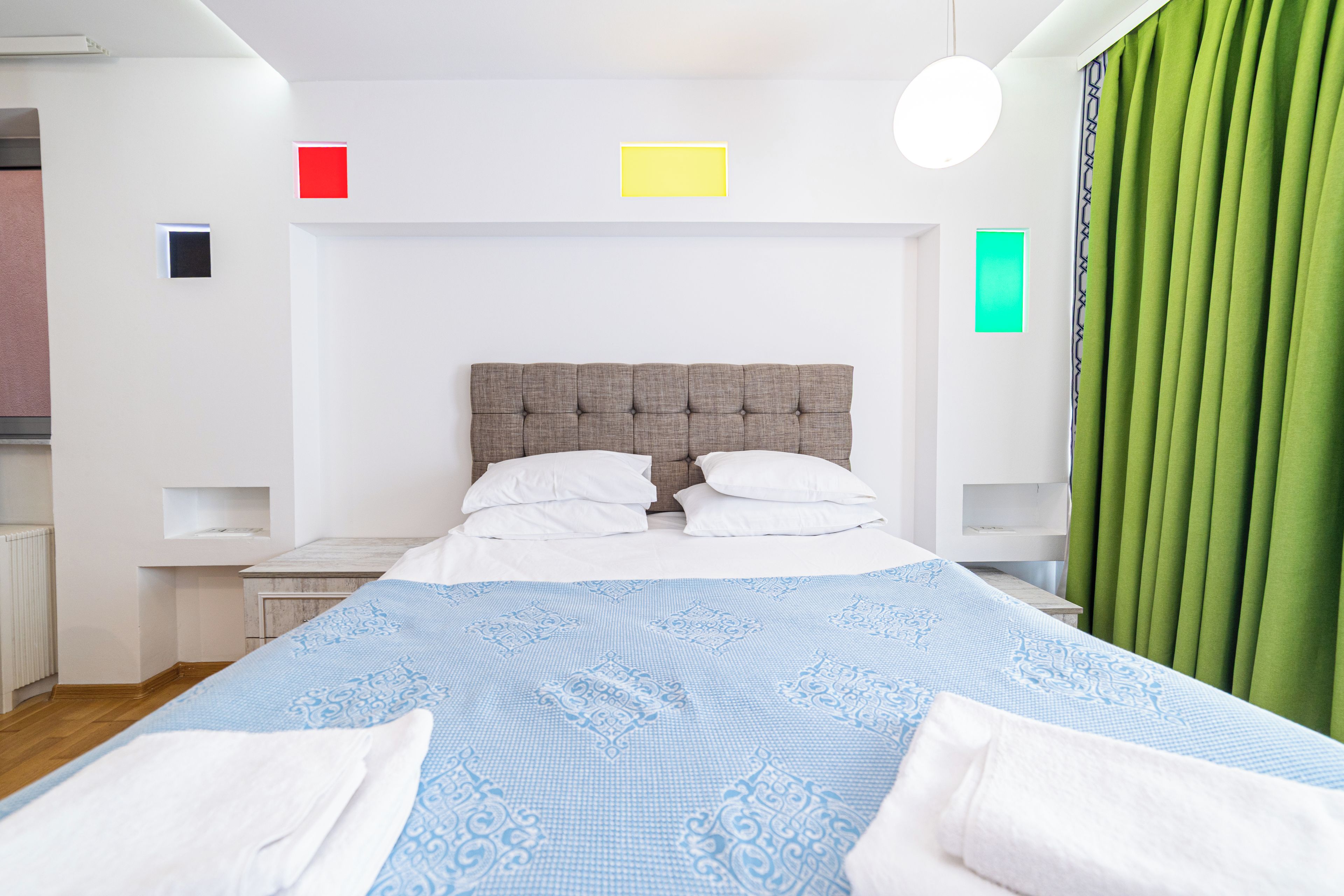 A hotel room with a large bed, two bedside tables, a headboard, and a green curtain.