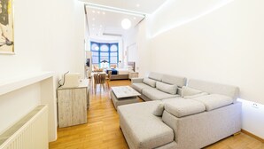 Una sala moderna con un sofá seccional, una mesa de comedor con sillas y una cocina al fondo.