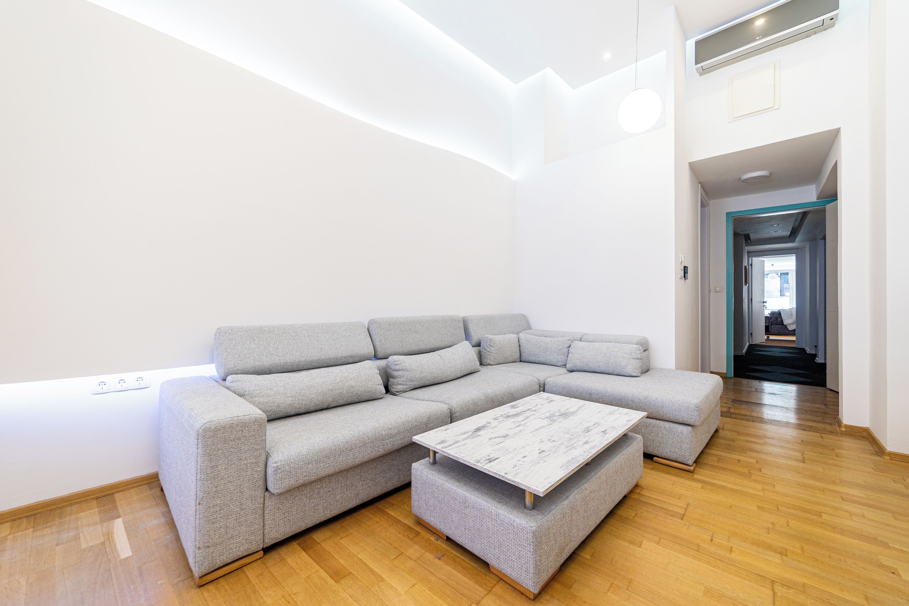 Ein modernes Wohnzimmer mit einem grauen Ecksofa, einem weißen Couchtisch und Holzböden.