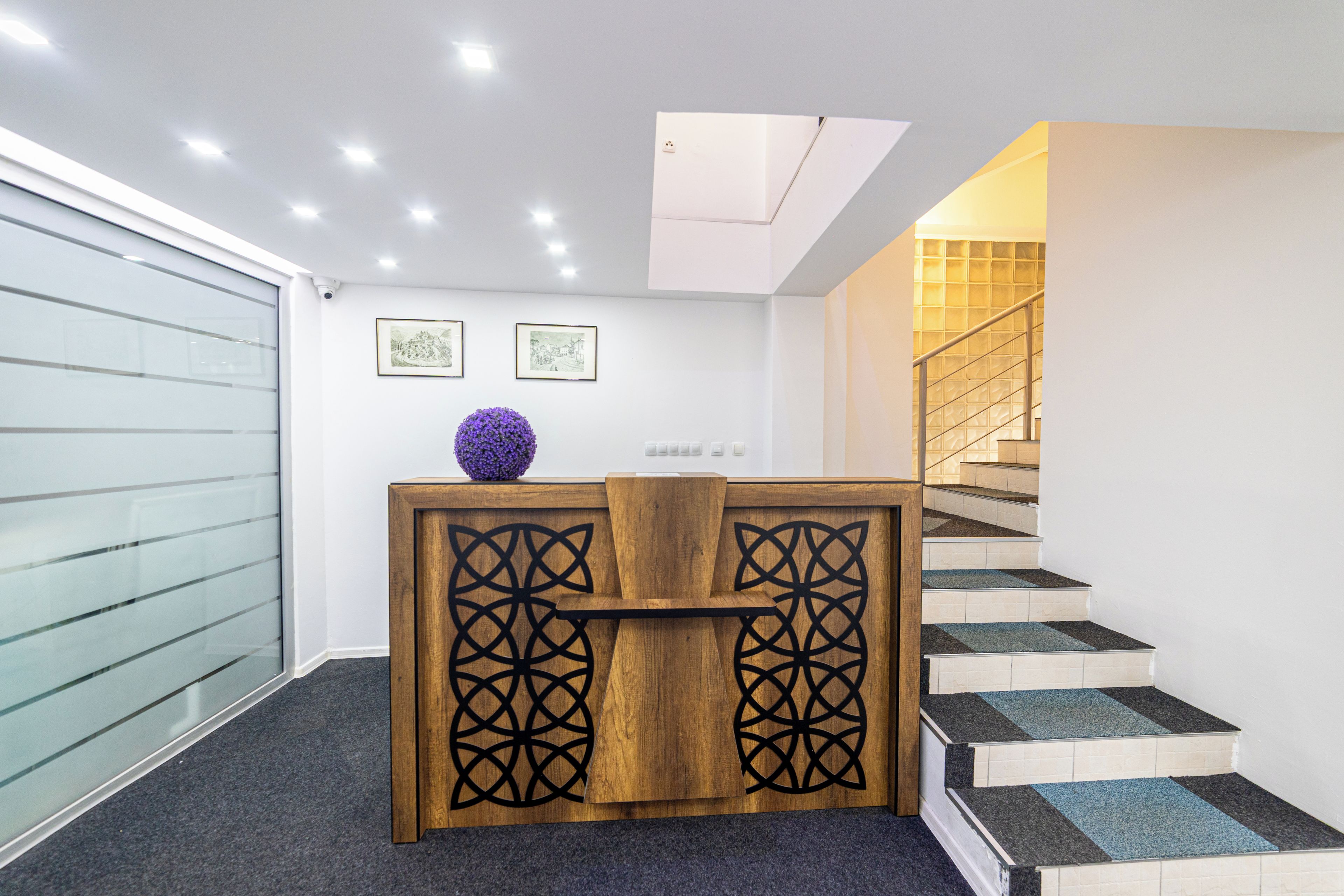 A reception desk with a wooden design and a purple decorative element, a staircase with patterned steps, and two framed pictures on the wall.