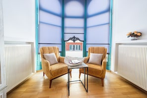 Una habitación con dos sillones, una mesita y vistas a través de un ventanal con marco azul.