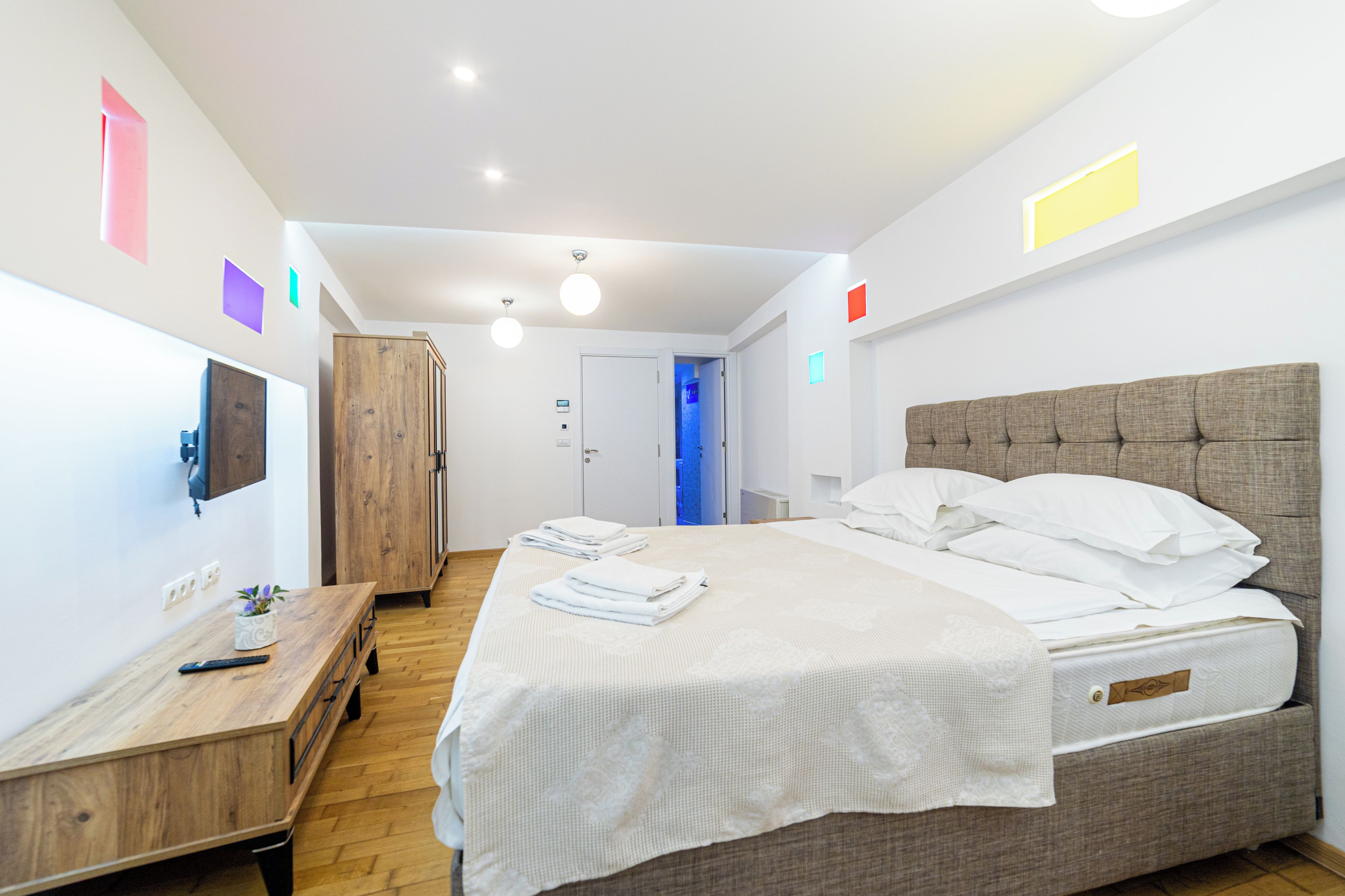 A hotel room with a bed, bedside table, wardrobe, and a view into the hallway.