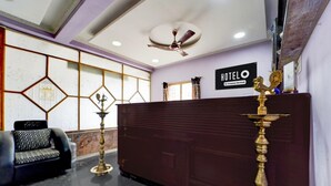 A hotel reception area with a reception desk, a seating area with a sofa, a ceiling fan, and a wall with a geometric pattern. - Deluxe kk Residency (Karaikal)